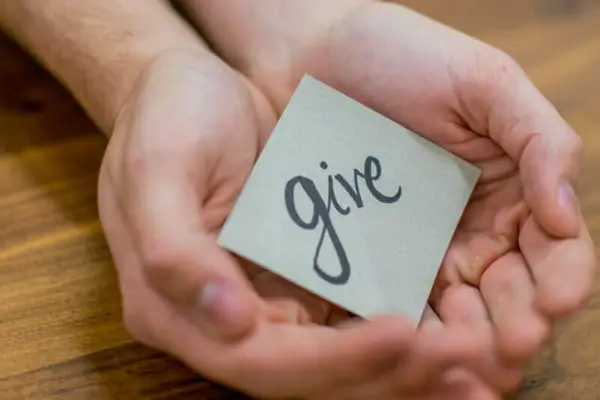 Hands holding a note with the word 'give', symbolizing the spirit of giving back at a Charlotte treatment center.