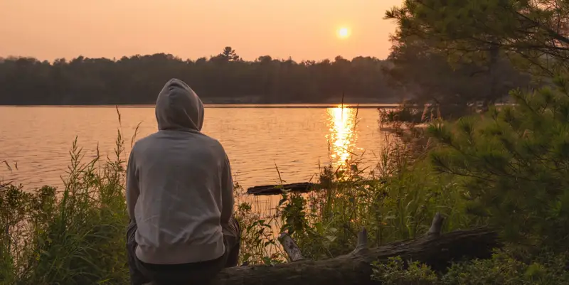 Person reflecting by a lake at sunset, representing addiction treatment and relapse prevention at Dilworth Center in Charlotte, North Carolina.