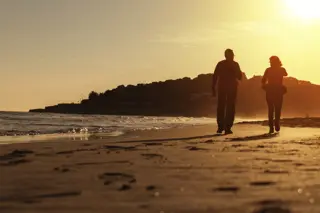 Couple enjoying a sober living lifestyle walking on the beach at sunset, highlighting a serene and healthy environment.