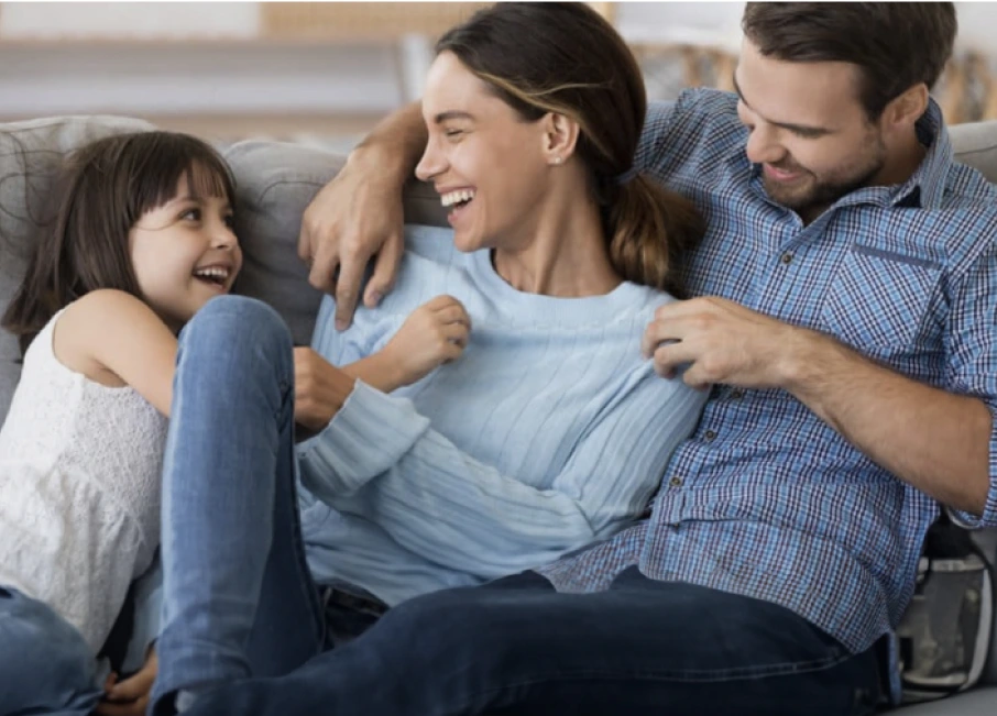 Family of a Husband, Wife, and Daughter laughing and playing on a couch