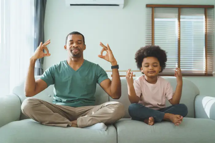 A father and child meditating together on a couch, symbolizing the role of family therapy in drug addiction recovery for young adults.