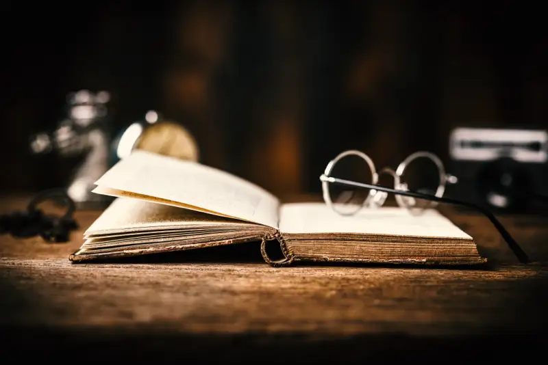 An open vintage book with reading glasses placed beside it on a wooden table, symbolizing the historical context and first recorded issues related to benzo addiction and withdrawal.