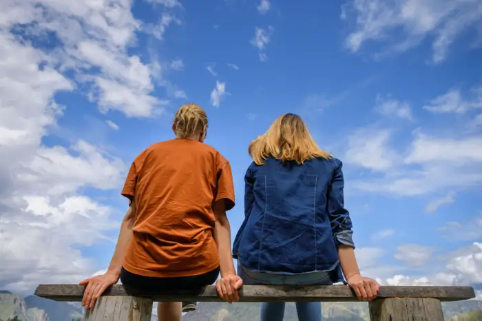 Two individuals sitting on a bench, gazing at a bright blue sky, symbolizing the importance of family support in the rehabilitation journey for young adults and teenagers.