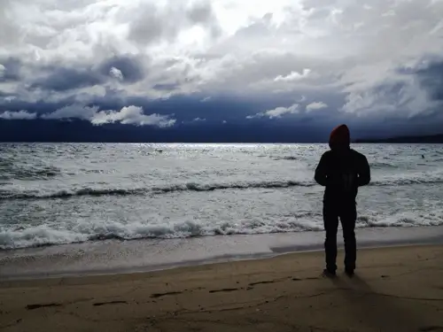 A person standing alone on a beach, gazing at a cloudy and turbulent sea, symbolizing the introspective journey of quitting weed and dealing with the side effects of cannabis.