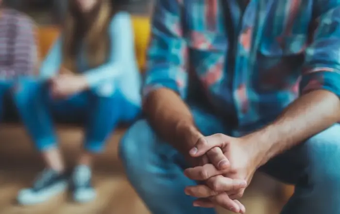 Close-up of a man's clasped hands in a support group, reflecting the struggle and support during narcotic withdrawal and recovery from opiate addiction.