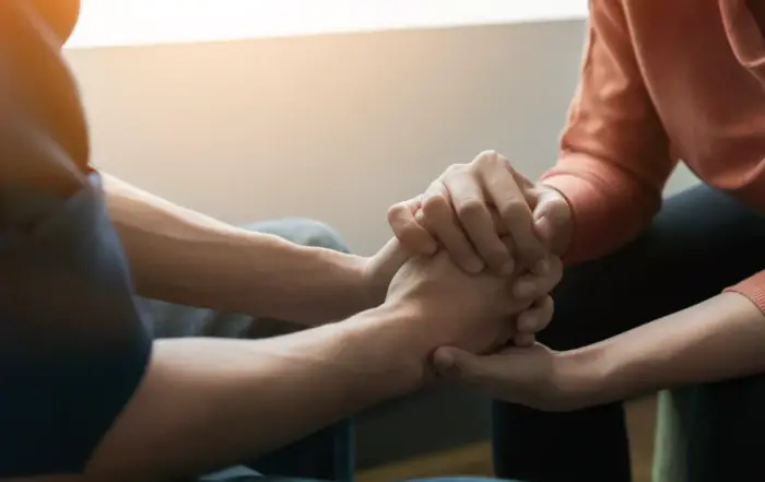 Four people joining hands in a circle at a support group session, symbolizing unity and support for overcoming marijuana addiction and related mental health disorders.