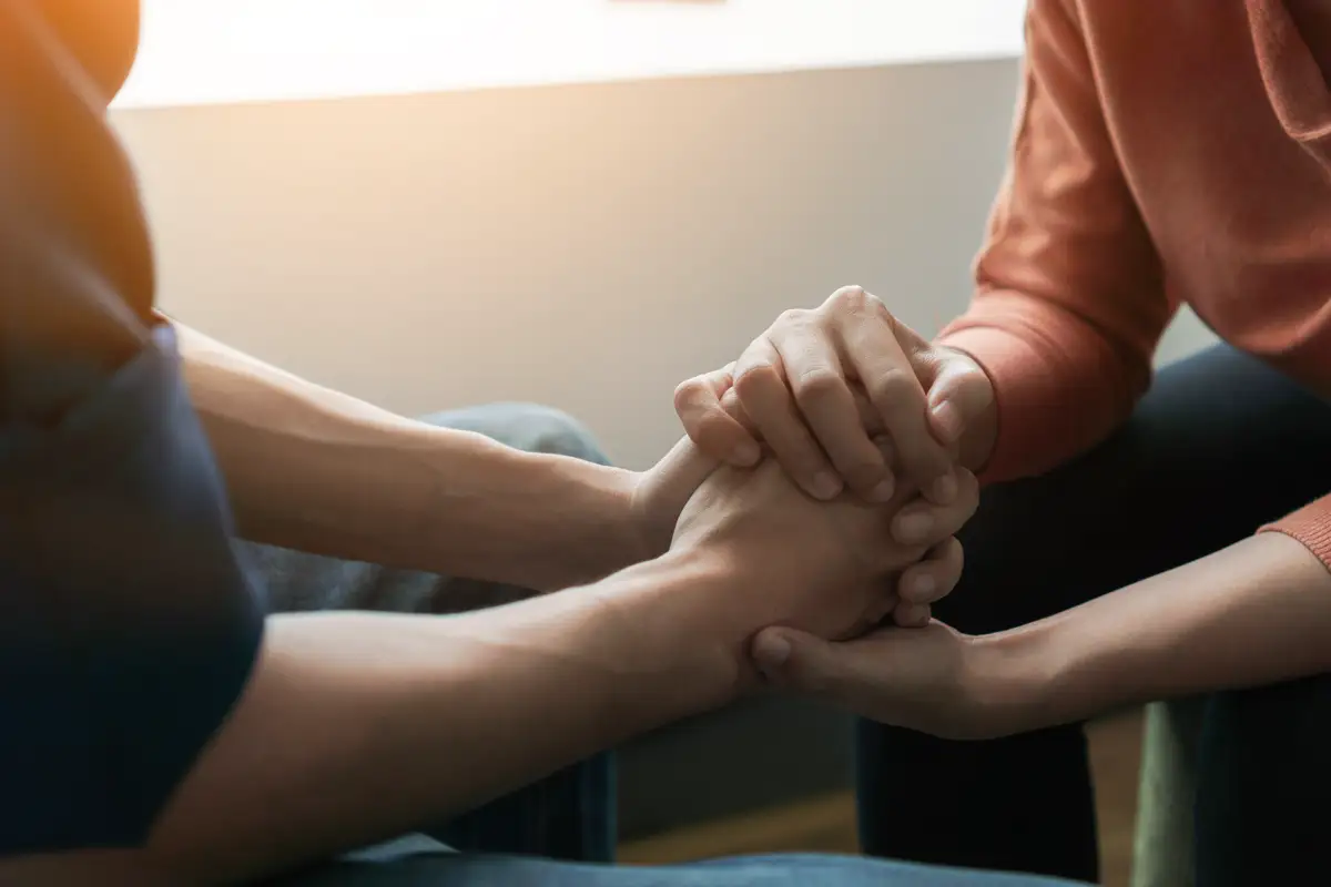 Four people joining hands in a circle at a support group session, symbolizing unity and support for overcoming marijuana addiction and related mental health disorders.