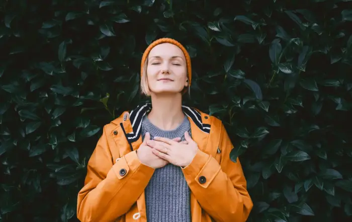 Woman in orange jacket meditating peacefully against a green leafy background, illustrating natural methods of calming anxiety without benzos.