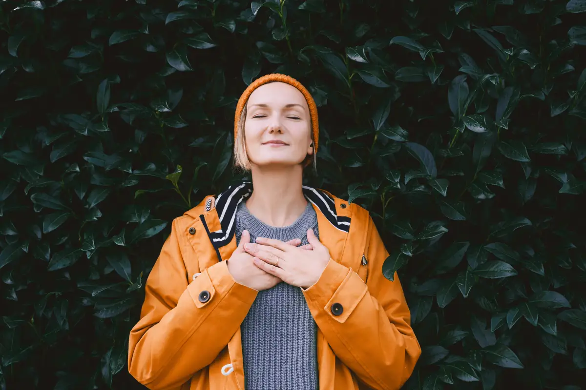 Woman in orange jacket meditating peacefully against a green leafy background, illustrating natural methods of calming anxiety without benzos.