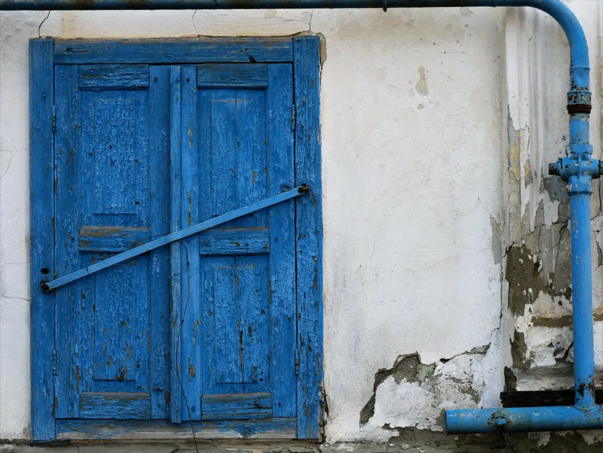 An old blue shuttered window on a weathered wall, illustrating methamphetamine withdrawal symptoms.